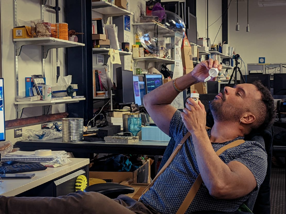 Person sitting at desk in lab space, leaning back in chair to blow bubbles.