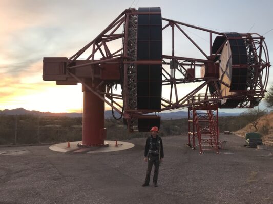 A man with a hard hat standing in front of the prototype Schwarzschild-Couder telescope at the Fred Lawrence Whipple Observatory