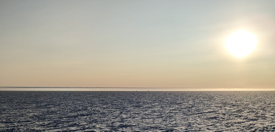 Huge bright sun over rough surface of South Pole, with mirage (Fata Morgana) on horizon.