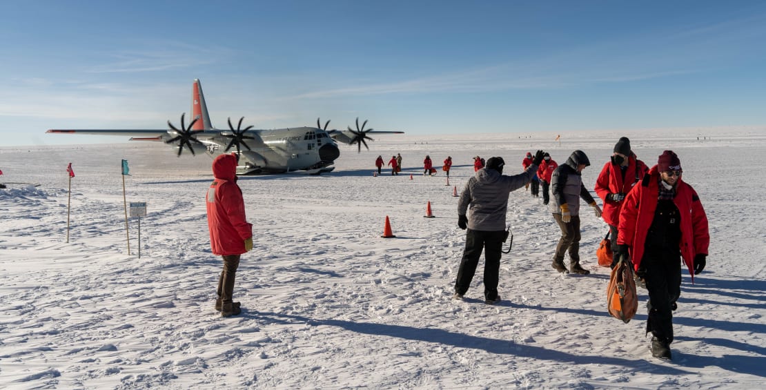 Crew departing plane, parked on ice in background.