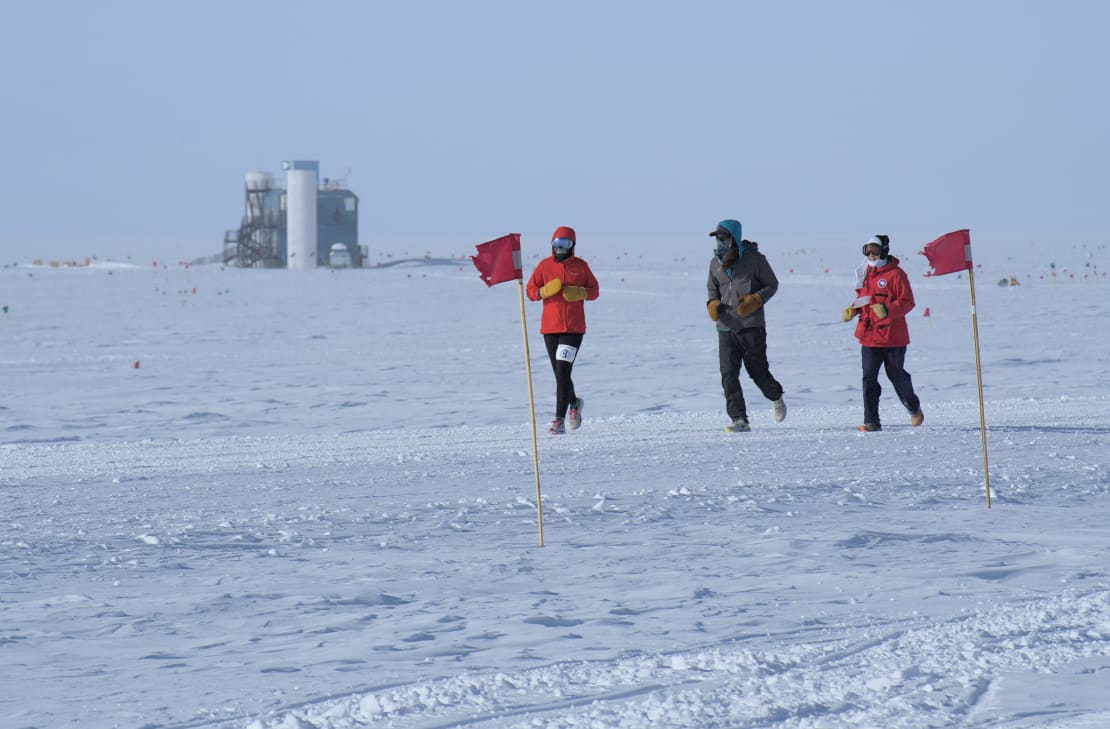 Three South Pole marathoners with IceCube Lab in distance.