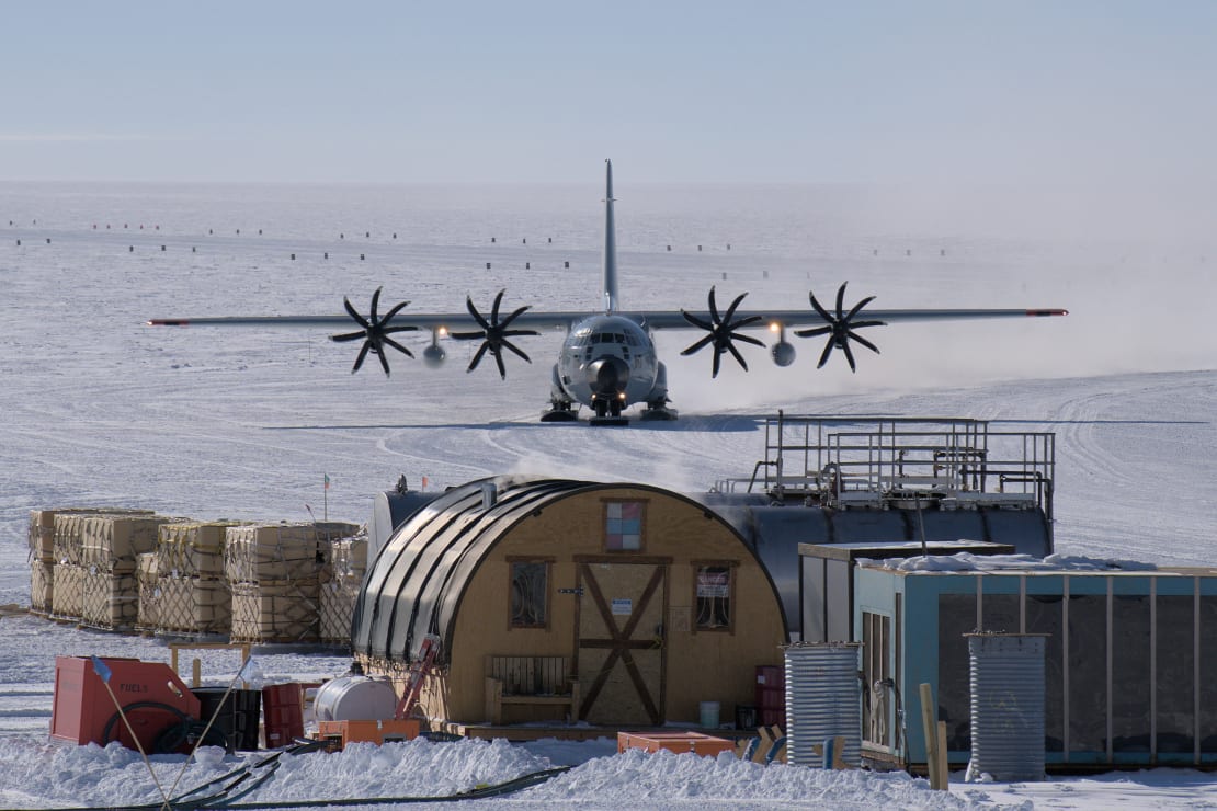 Front view of large plane taxing behind fuel buildings.