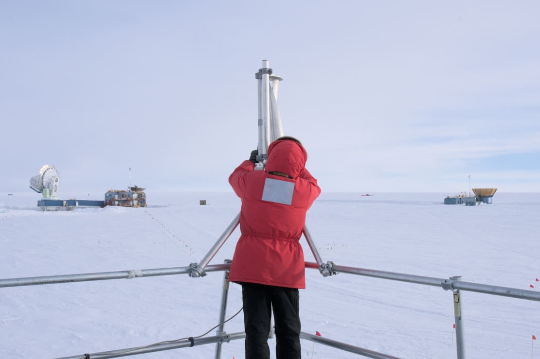 Rear view of person in red parka working on an outdoor repair at the South Pole.