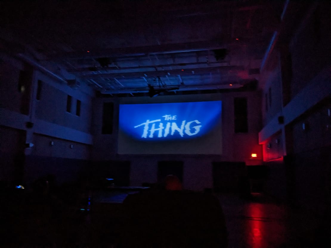 View of title screen of “The Thing” projected onto screen in dark gym.