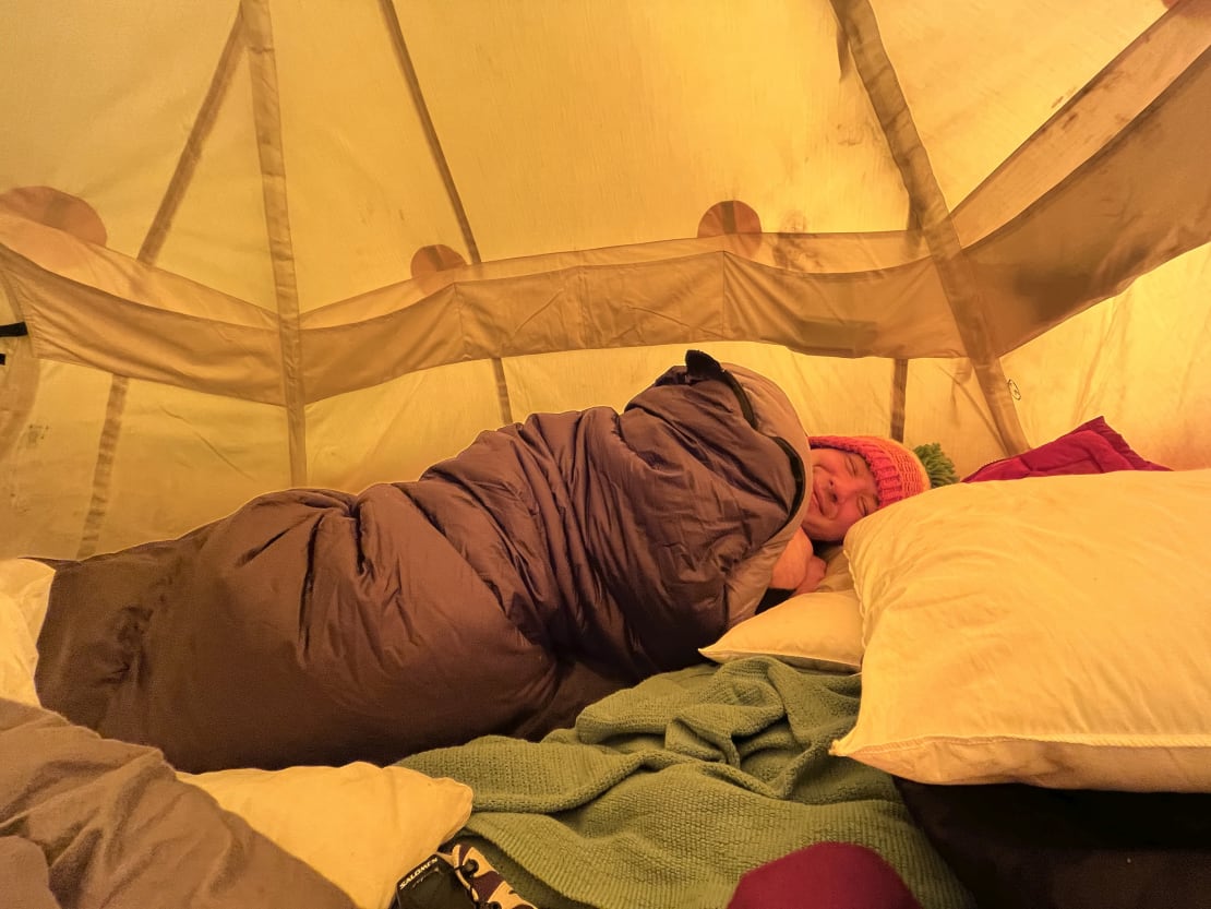 Person smiling with eyes closed, bundled in sleeping bag inside a Scott tent at the South Pole.