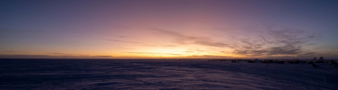 Panoramic view of horizon just after sunset at the South Pole, with a few wispy clouds off to the side.