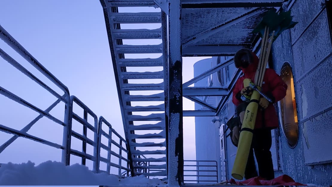 Winterover standing below staircase at the IceCube Lab at twilight.