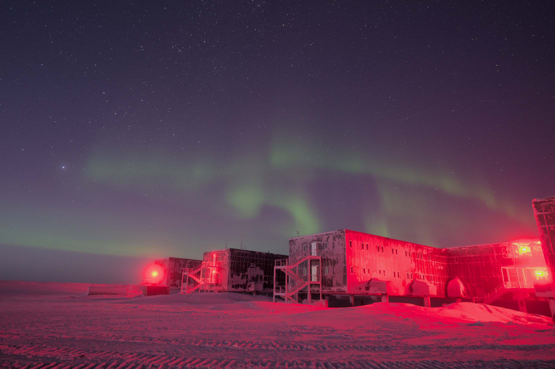 Faint green auroras over the South Pole station, lit in red.