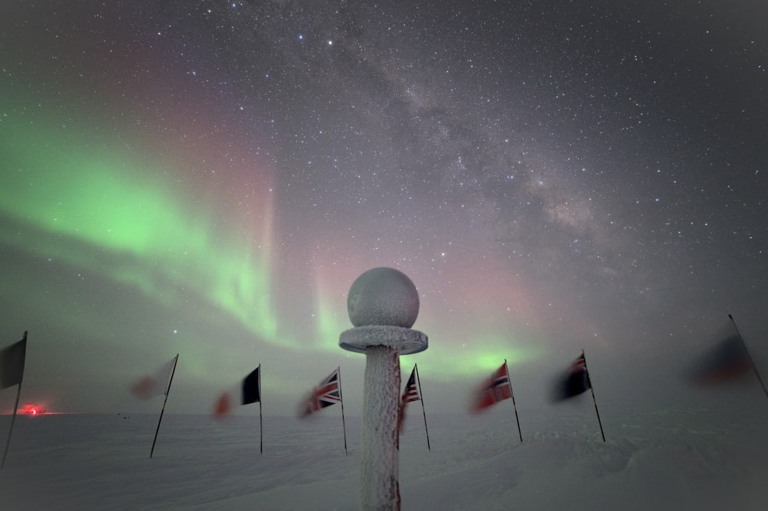 Frosted globe marker at ceremonial South Pole, starry night sky and auroras as backdrop.