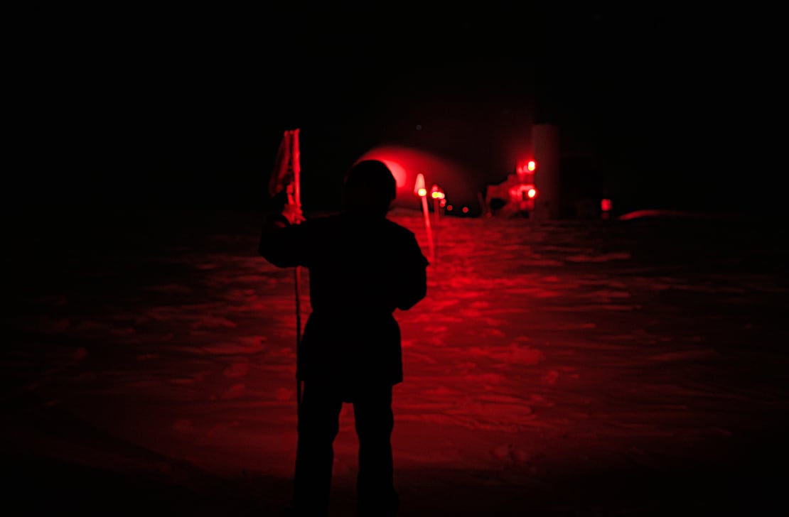 Person in shadow in dark scene lit only by red headlamp, showing some flags lit up.