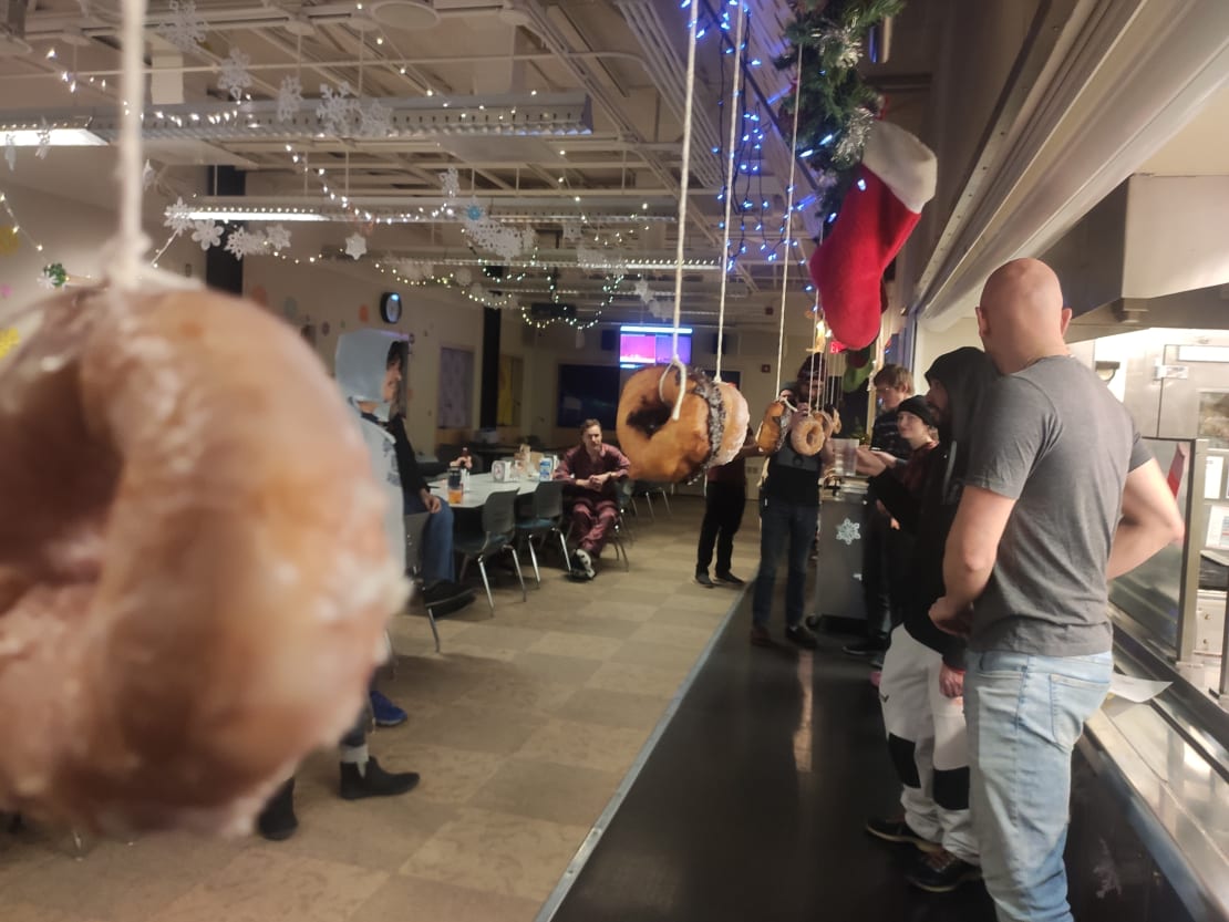 Long view of donuts hanging from strings for a donut eating contest, with people waiting in the wings.