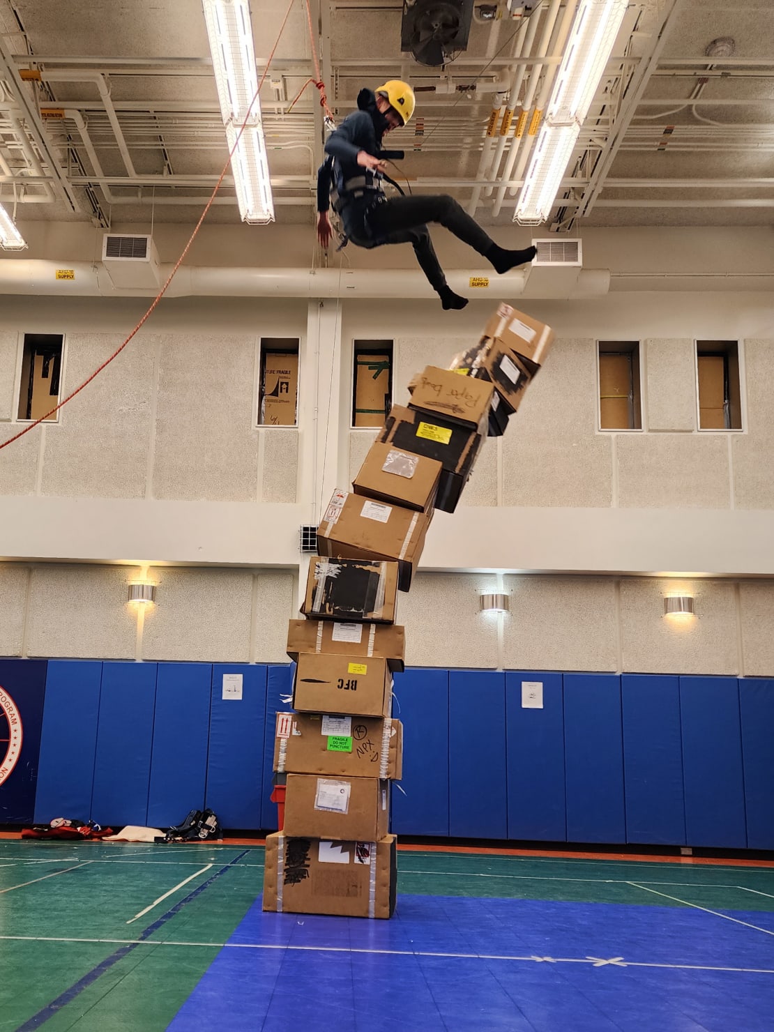 Person hanging in mid air from ceiling harness as they fall off of toppling tower of cardboard boxes.