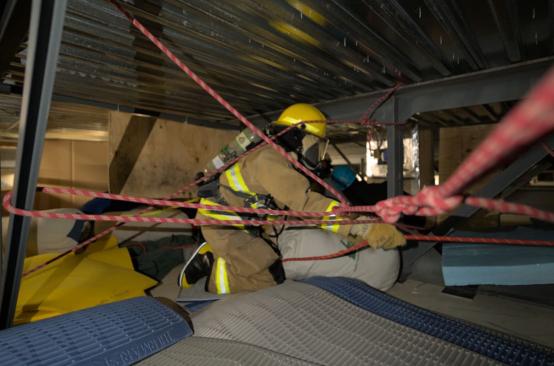 Person in firefighter gear navigating obstacle course in crawlspace.