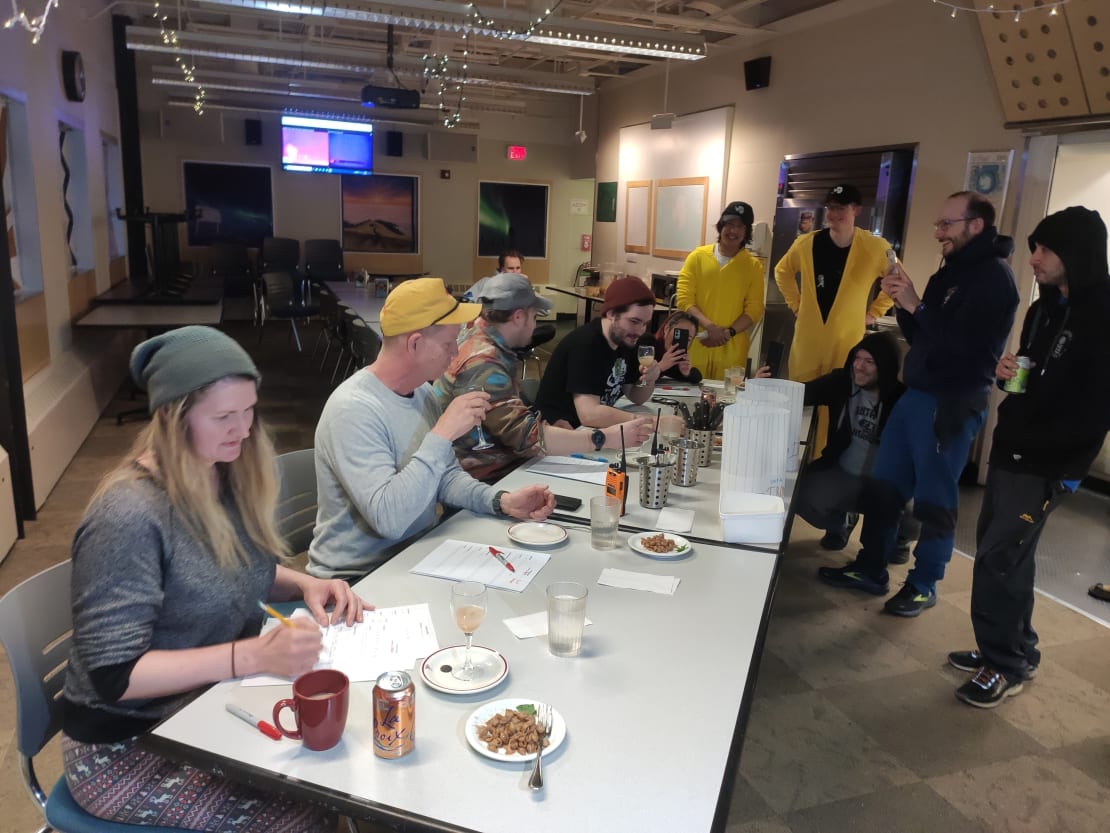 Long table with judges eating and rating prepared dishes, a few onlookers.