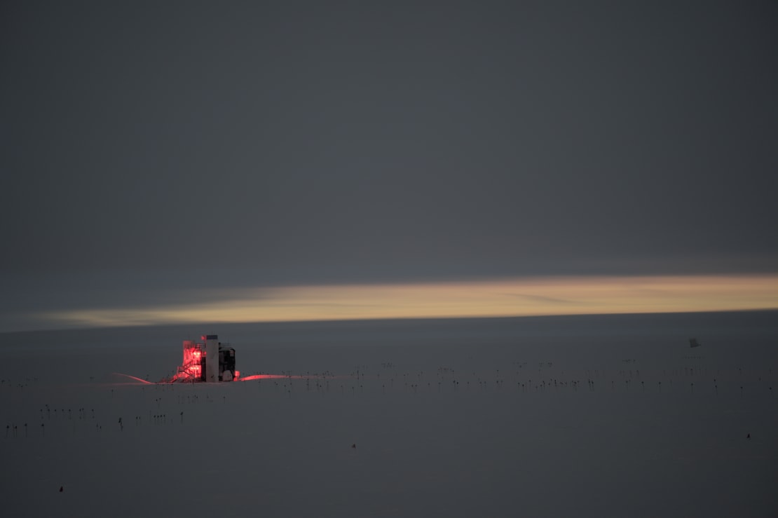 Faint glow along horizon with IceCube Lab in distance still lit in red lights during winter-summer twilight.