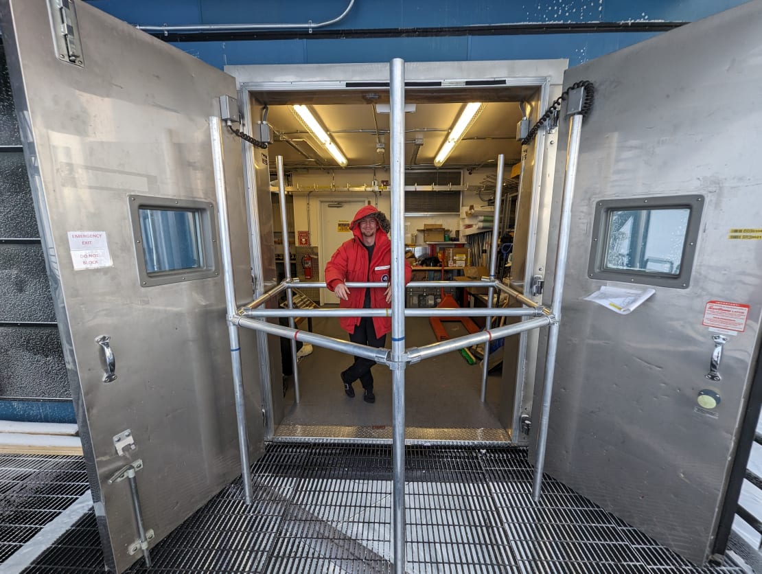 Person in red parka pushing a metal frame through the opened exterior doors of the IceCube Lab.