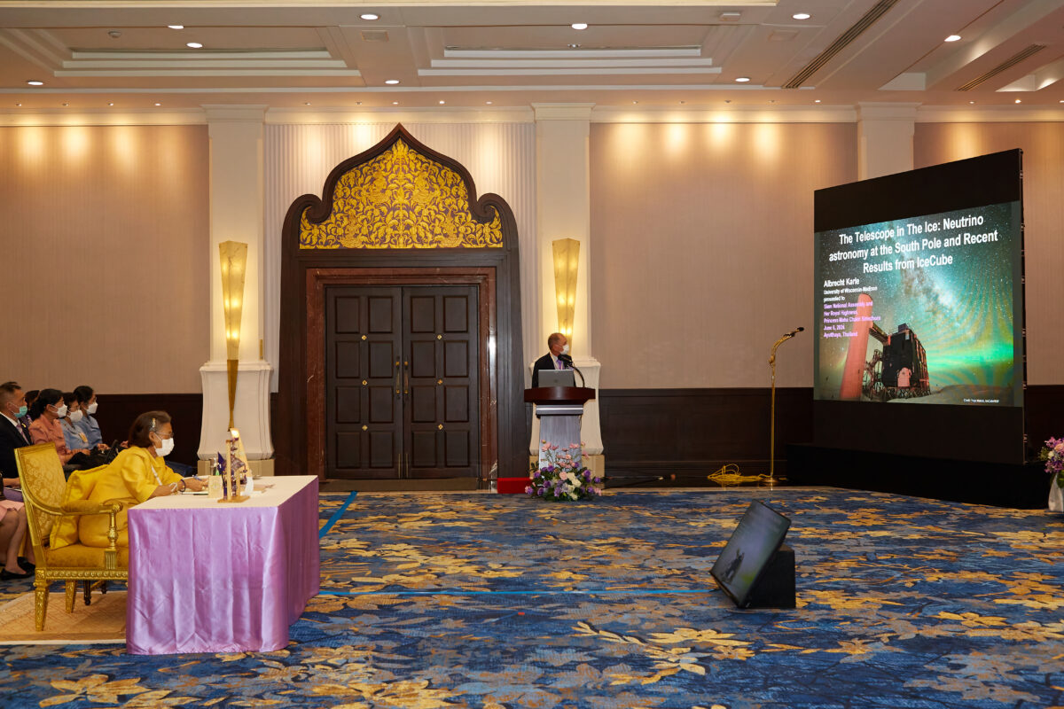 A person talking in front of a big screen with people sitting in chairs and someone sitting at a table