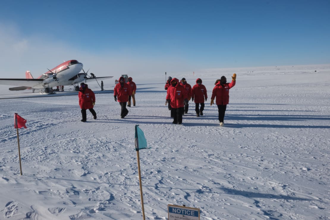 Group in red parkas walking away from plane toward the camera.