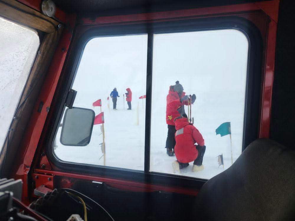 Several people in red parkas working outside at the South Pole, viewed from inside the snow vehicle.