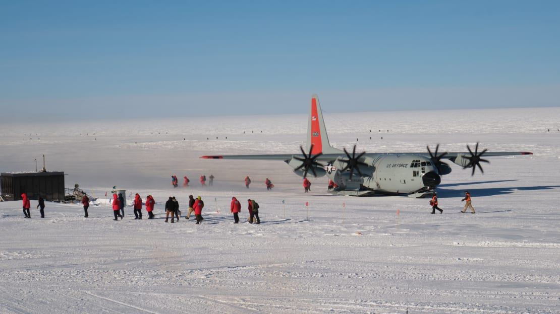 An LC-130 on the skiway at the South Pole, with lines of people in red parkas walking away from it.