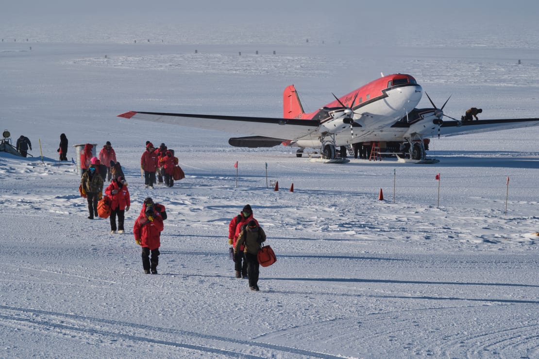 Plane parked on skiway, with disembarking passengers in red parkas walking away from it.